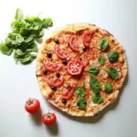 Cheese pizza topped with fresh tomato slices and spinach leaves