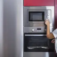 person opening the door of a stainless steel microwave in a modern style kitchen