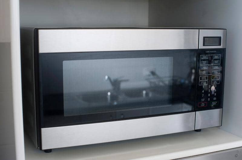 Closed microwave oven standing on kitchen shelving for efficient reheating and cooking