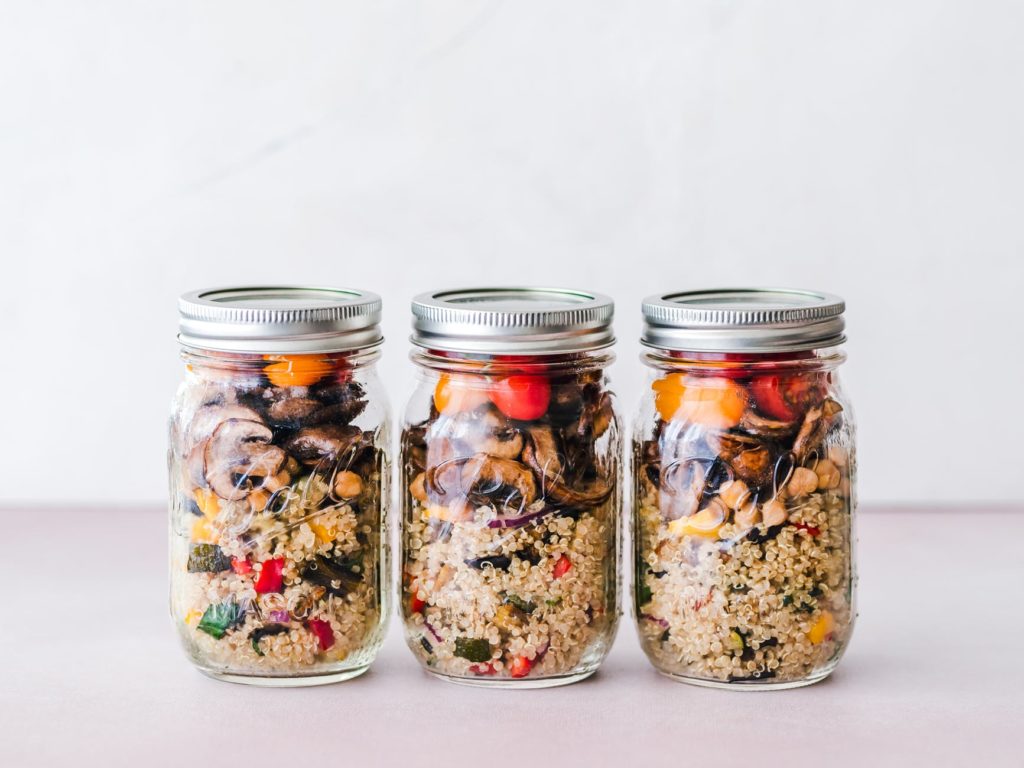 three mason jars filled with a simple meal prep of quinoa and assorted roasted vegetables