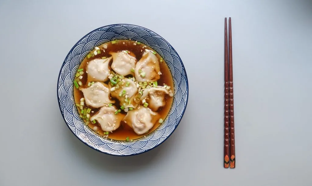 Blue bowl filled with dumpling soup and clear bone broth Blue bowl filled with dumpling soup and clear bone broth. Chopsticks are laying on the side.