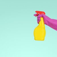 Hand wearing pink gloves hold a yellow spray bottle.