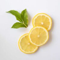 Three slices of lemon laying on a white tabletop with a spring of fresh mint.