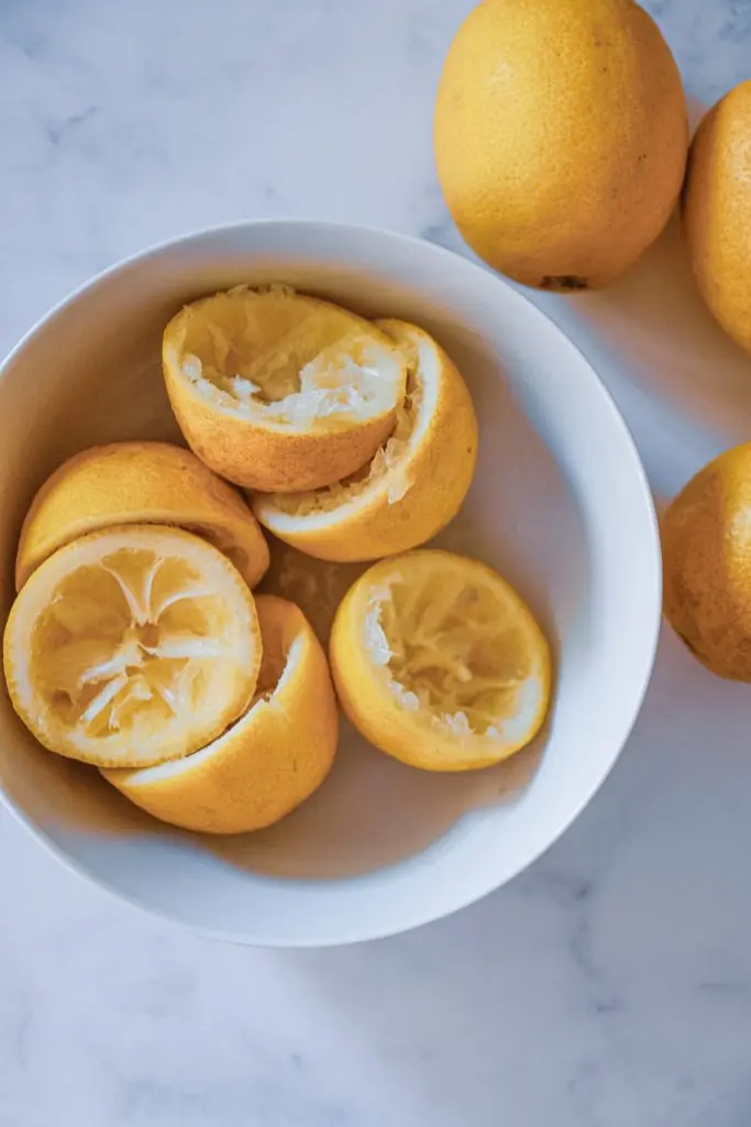 Whole lemons and juiced lemons Three whole lemons next to a small bowl with three lemons that have been cut in half and juiced.