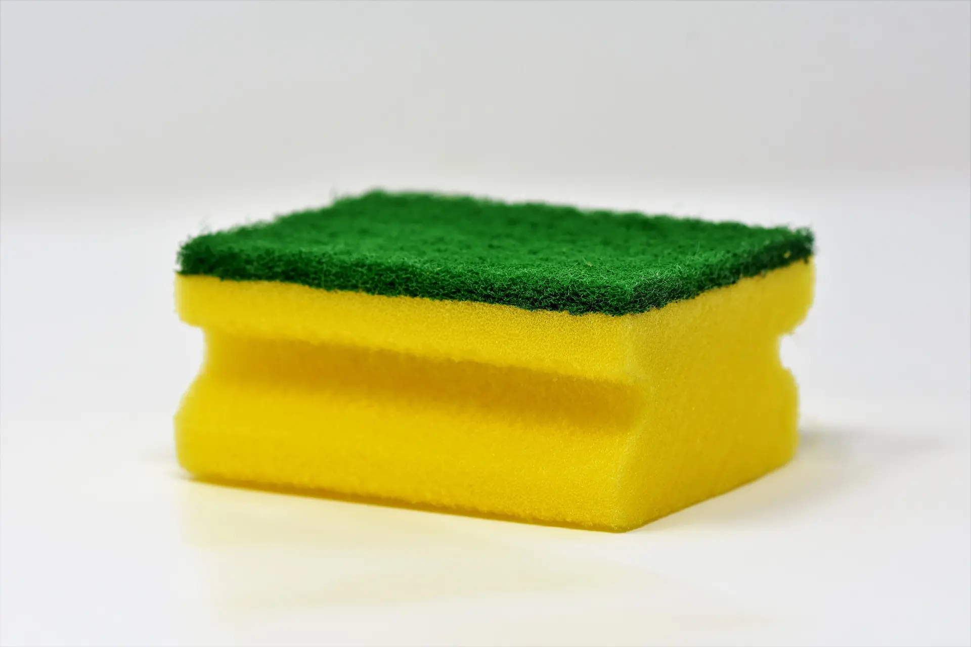 A yellow sponge with a green scrub pad on one side.